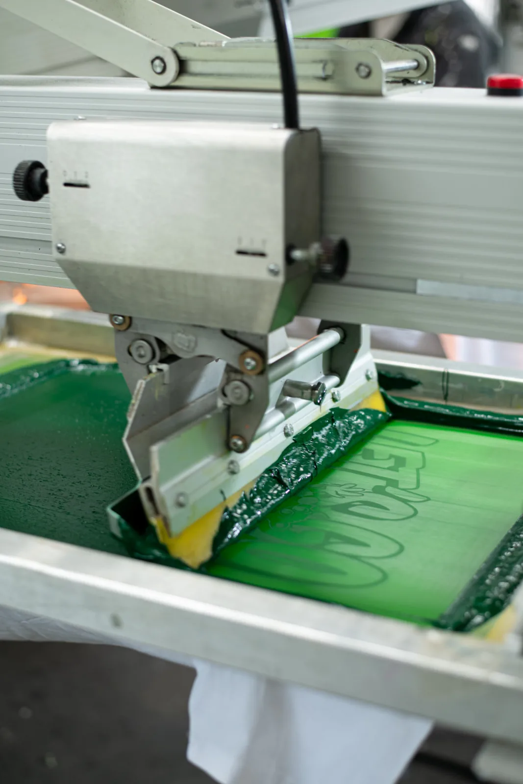 Automatischer Rakel druckt grüne Siebdruckfarbe auf ein Textil, TIME/LESS Prints.
