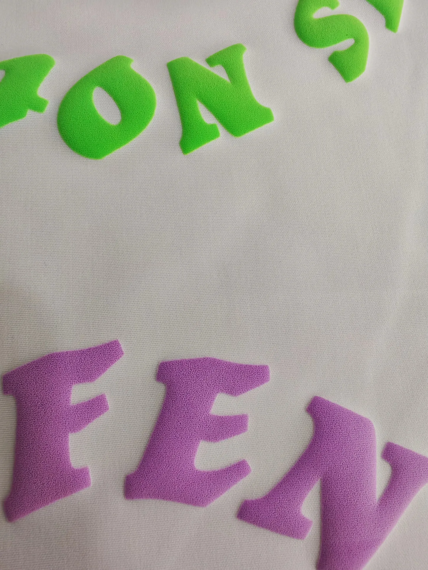 Puff-Druck-Lettern in Neongrün und Lila auf hellem Textil, TIME/LESS Prints Hannover.