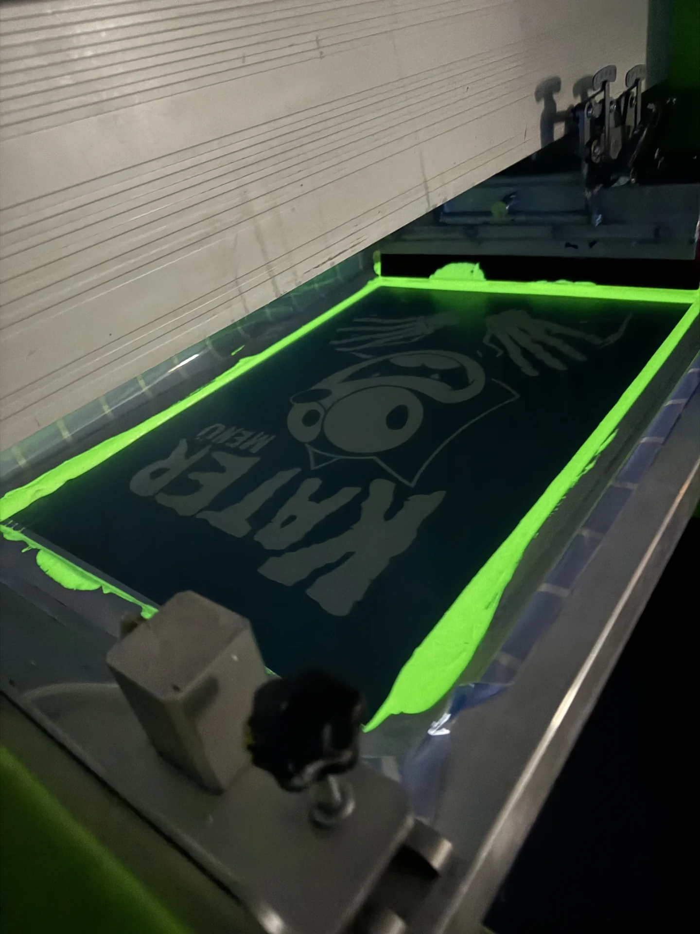Sieb mit nachleuchtender Glow-in-the-Dark-Farbe auf der Siebdruckmaschine im Dunkeln, TIME/LESS Prints Hannover.