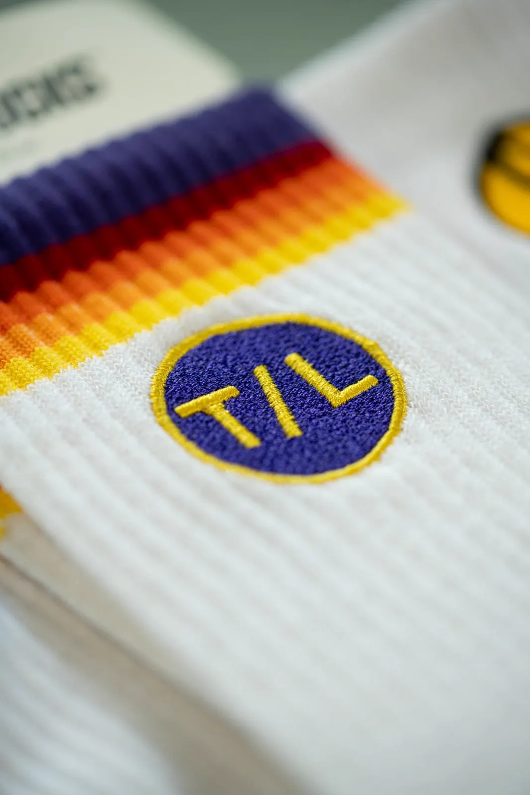 Bestickte Socke mit TIME/LESS-Logo in Lila und Gelb.