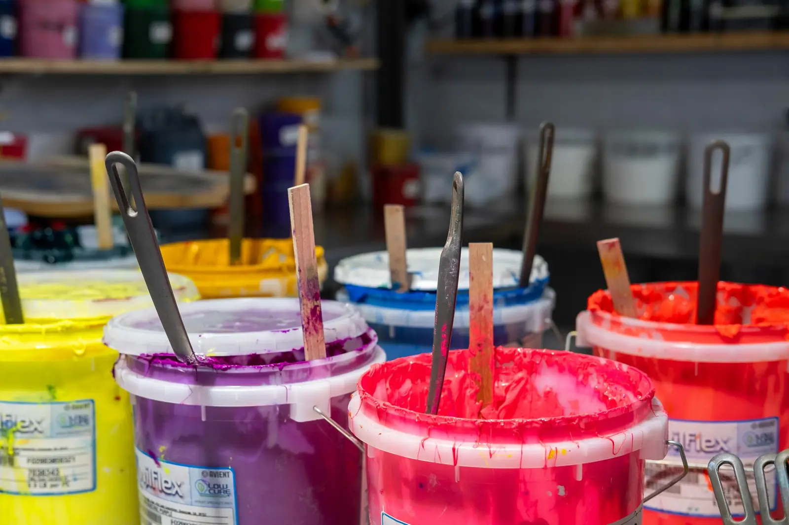 Bunte Siebdruckfarben in offenen Eimern mit Spateln.