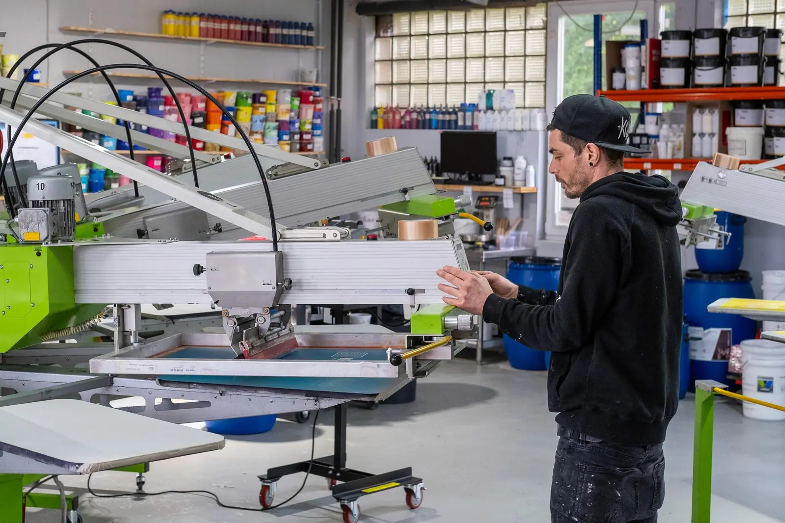 Mitarbeiter bedruckt ein T-Shirt an der Siebdruckmaschine bei TIME/LESS Prints in Hannover.