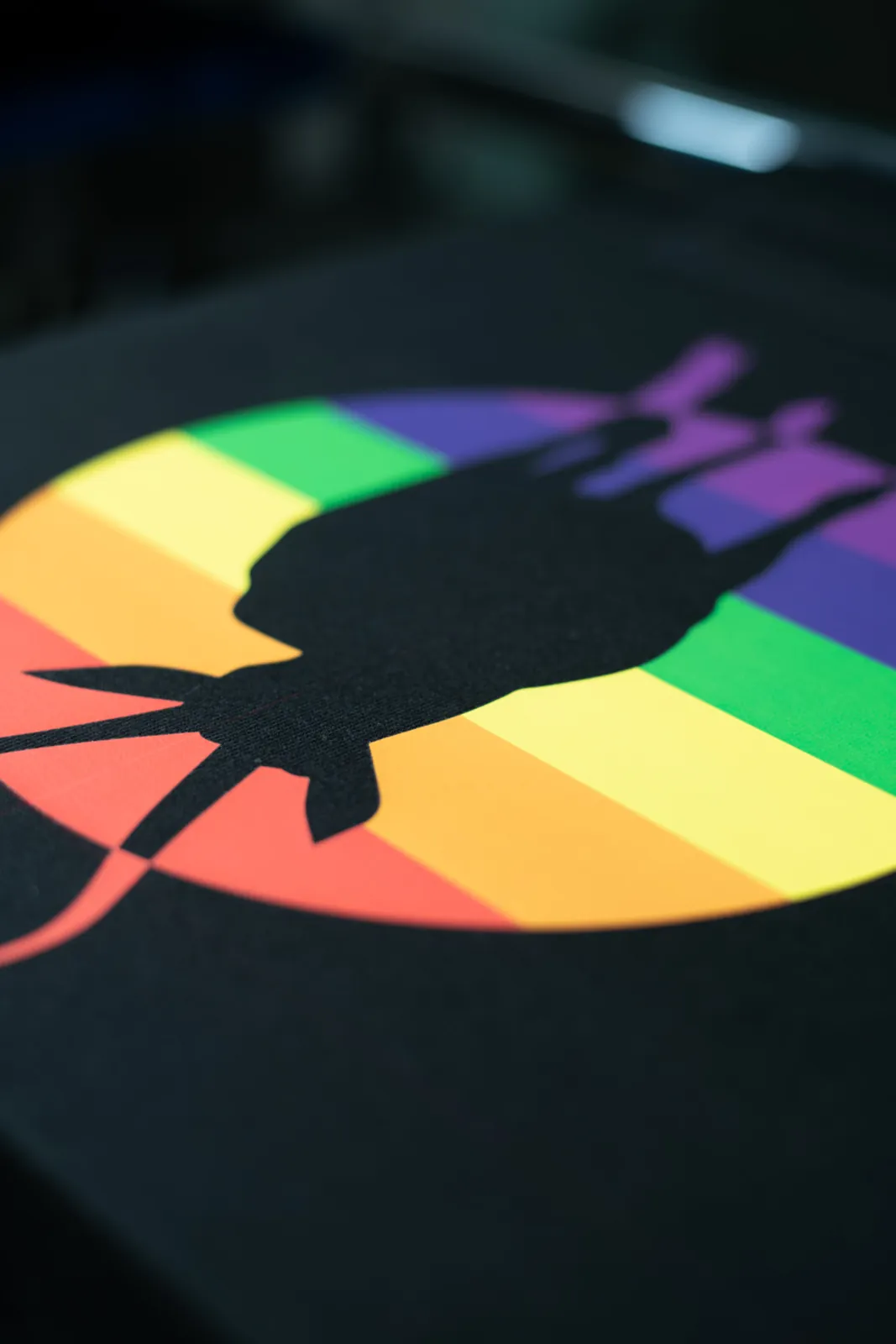 Detailaufnahme eines Regenbogen-Motivs im mehrfarbigen Siebdruck auf schwarzem Bandshirt, gedruckt bei TIME/LESS Prints.