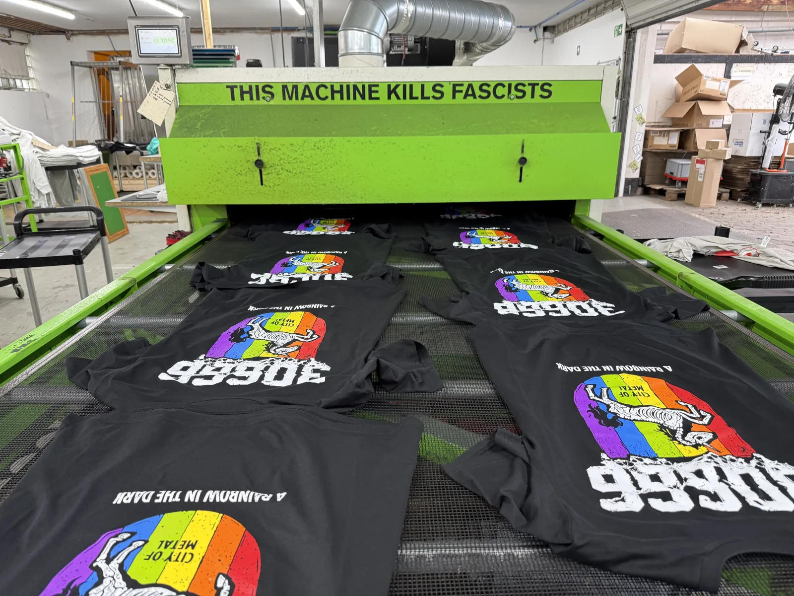Frisch bedruckte schwarze Bandshirts mit mehrfarbigem Regenbogenmotiv laufen im Siebdruck durch den Trockner bei TIME/LESS Prints.