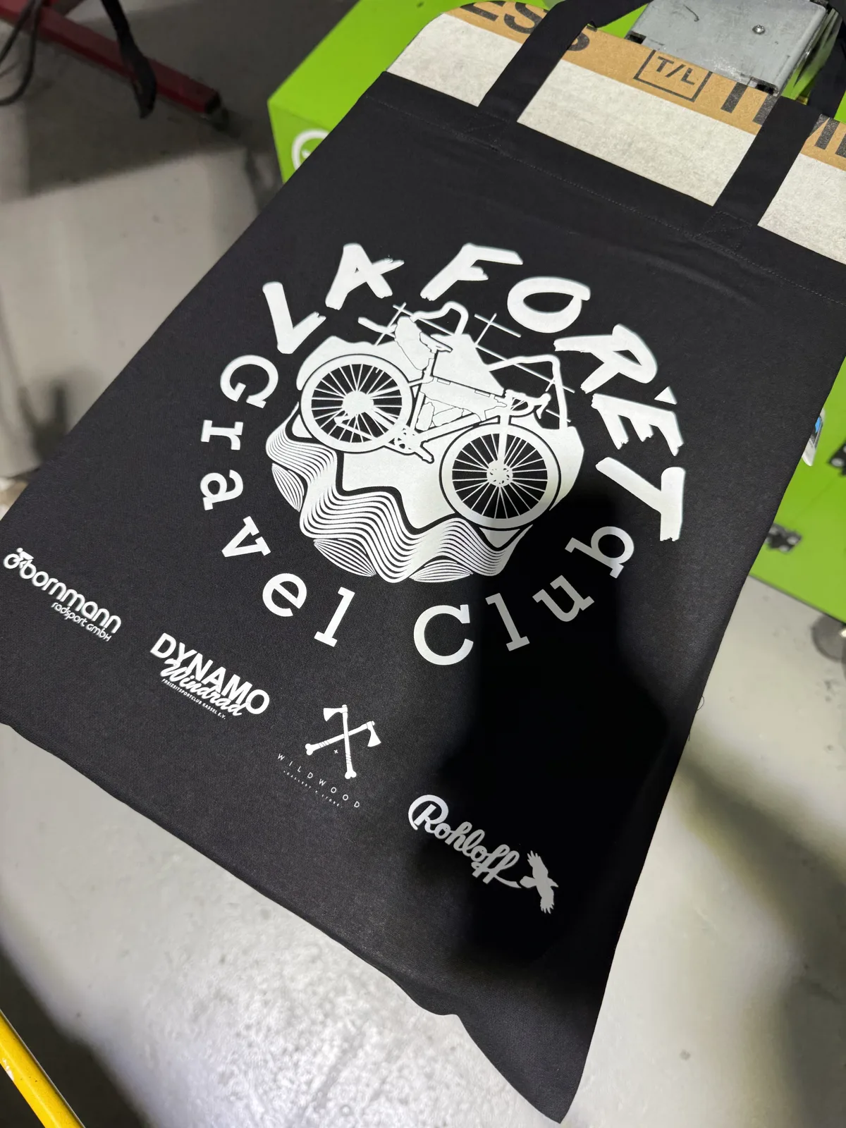 Schwarze Baumwolltasche mit weißem Gravel-Club-Motiv und Sponsorenlogos im Siebdruck bei TIME/LESS Prints.