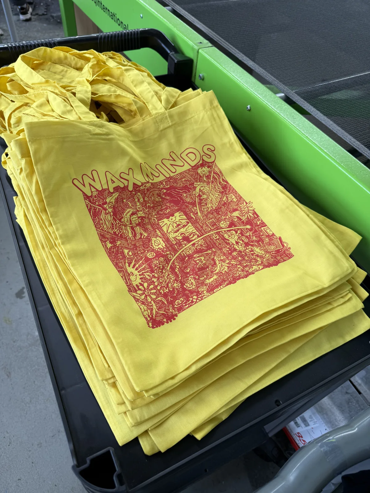 Stapel gelber Baumwolltaschen mit rotem Illustrationsmotiv im Siebdruck bei TIME/LESS Prints.