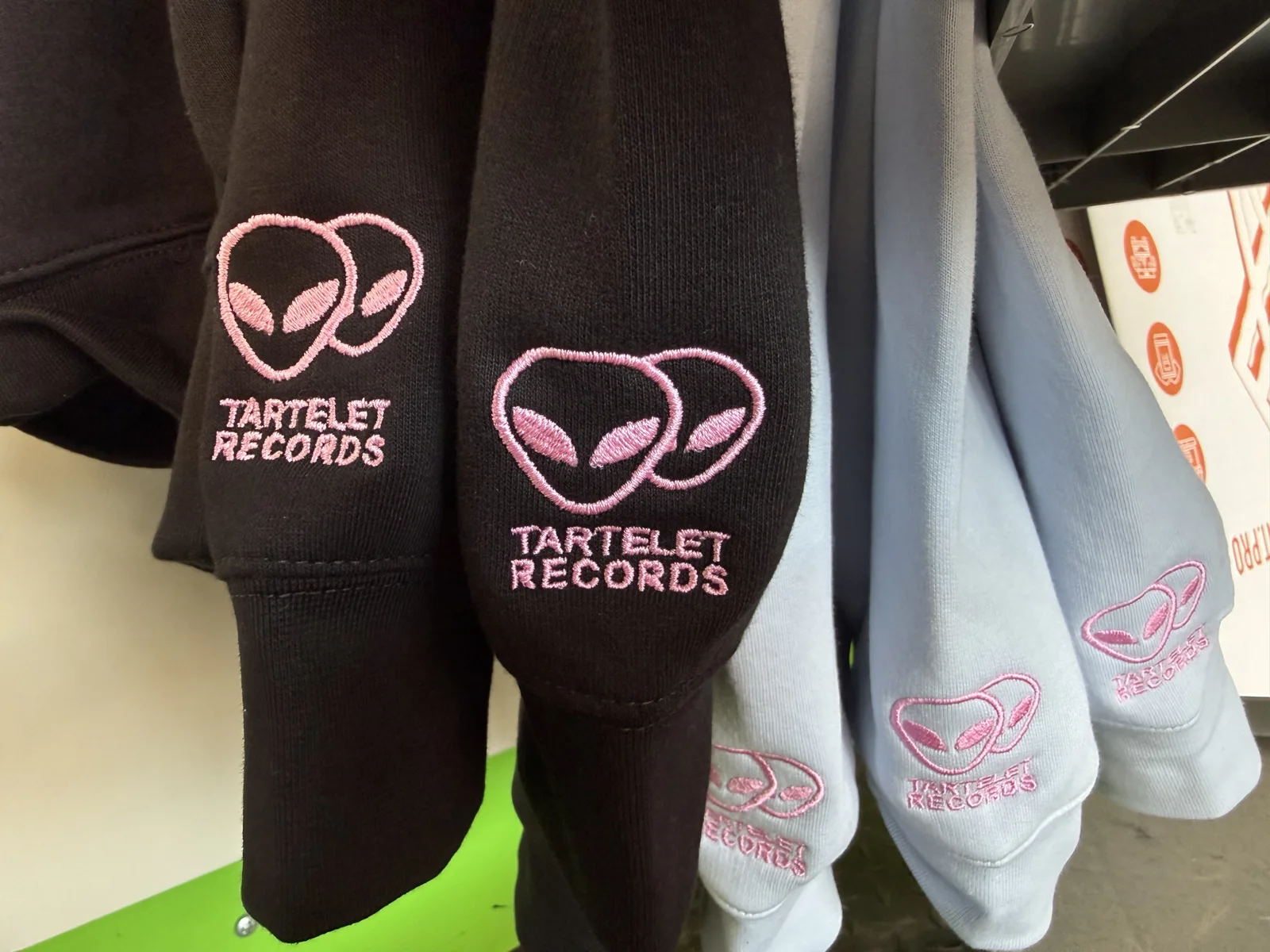 Schwarze und hellblaue Sweatshirts mit rosa Ärmelstick-Logo, Maschinenstick bei TIME/LESS Prints.