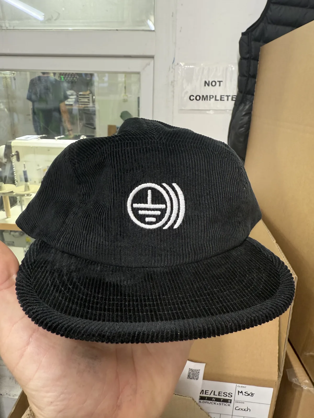 Schwarzes Cord-Cap mit weiß gesticktem Logo, Maschinenstick bei TIME/LESS Prints.