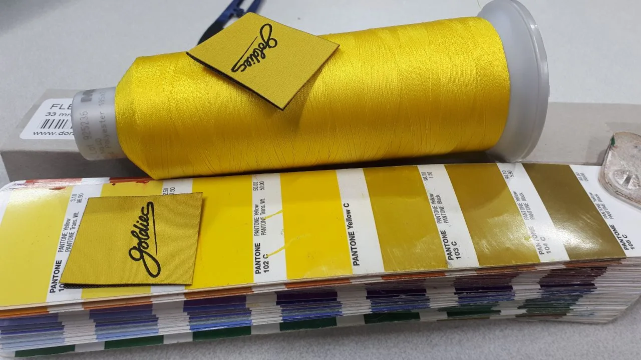 Gelbe Garnkone mit Stickmuster und Pantone-Fächer zur Farbabstimmung für Maschinenstick bei TIME/LESS Prints.